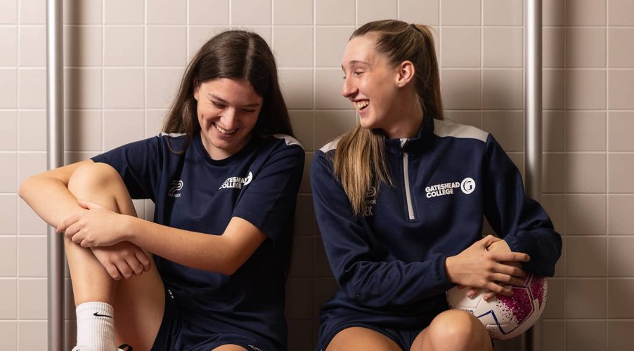 Two women's football academy students sat on bench, laughing